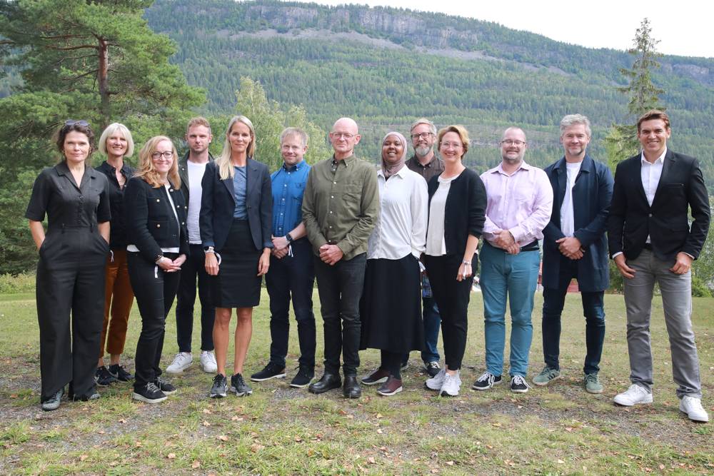 Bilde av Ekstremismekommisjonen på Utøya. I bakgrunnen er det trær og fjell. Det er 13 personer på bildet.