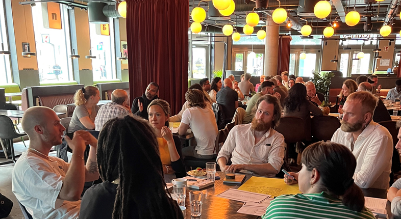 Bilde fra innspillsmøte 19. juni, deltakere ved flere bord diskuterer i grupper.