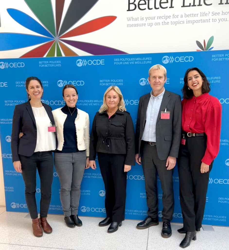 Five people standing in a line in front of an OECD photo backdrop.